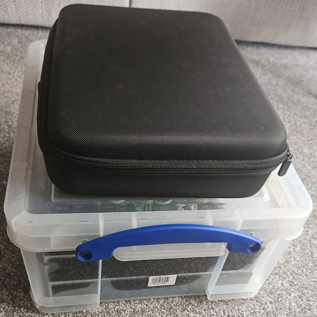 Black zippered case on top of a clear plastic storage box with a blue handle.
