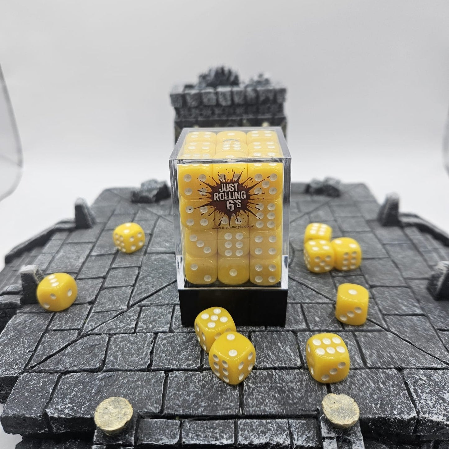 Yellow dice with white pips on a textured surface, with a clear container labeled 'Just Rolling 6's'.