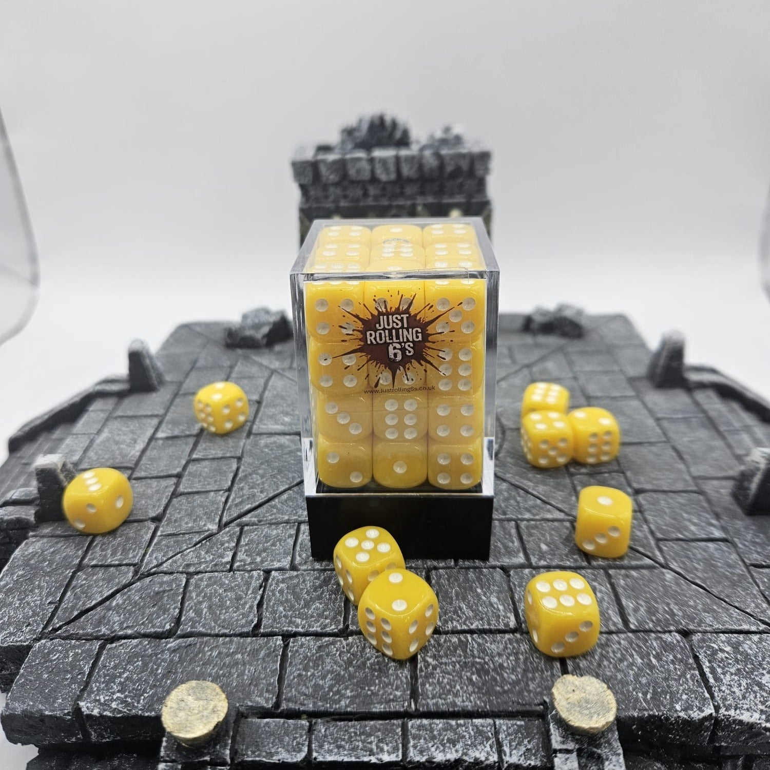 Yellow dice with white pips on a textured surface, with a clear container labeled 'Just Rolling 6's'.