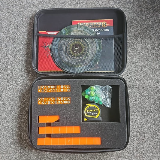 Black carrying case with compartments containing cards, dice, and tools on a gray surface